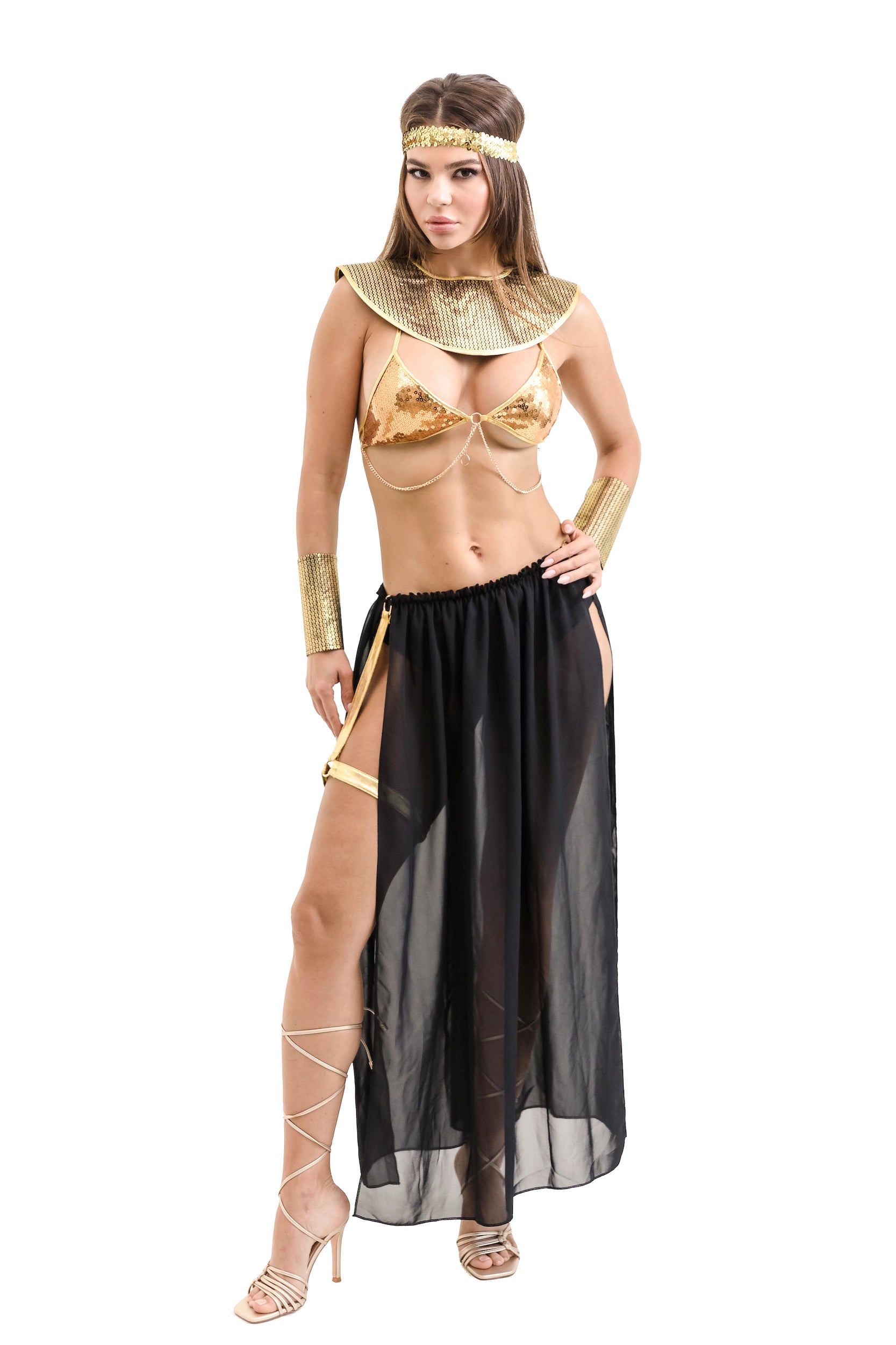 A woman modeling an Egyptian Queen costume, featuring a gold sequin bra top, black flowing skirt, headband, wristbands, and underpants. She is standing on one leg, showcasing the outfit's flow and design.