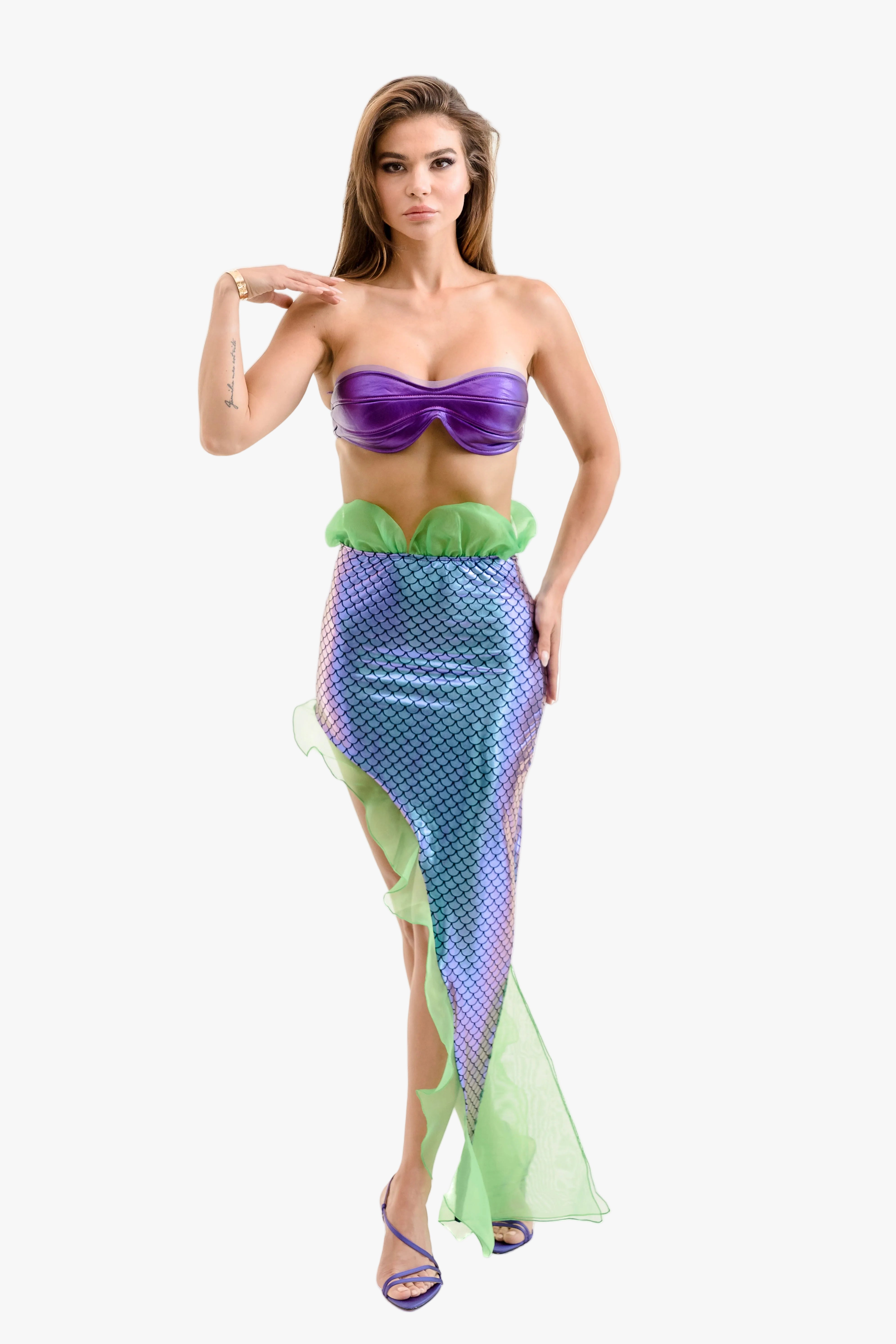 A woman modeling a mermaid costume consisting of a purple strapless top, a green ruffled waistband, and a blue-green scale-patterned skirt with a flowing green tail fin, set against a plain light gray background.