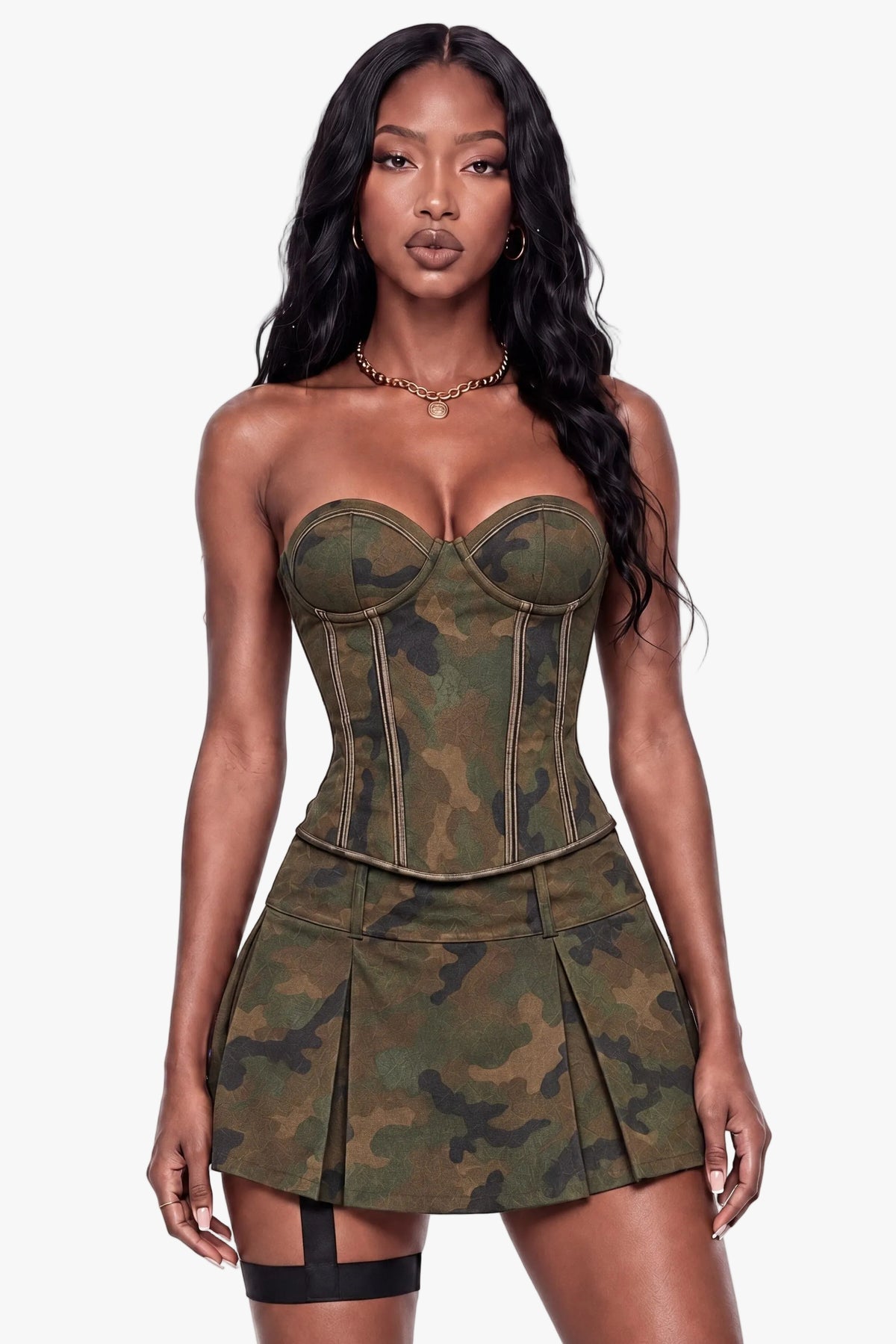 A woman modeling a strapless mini dress with a camouflage pattern and structured corset-style bodice, paired with black thigh-high stockings, against a plain white background.