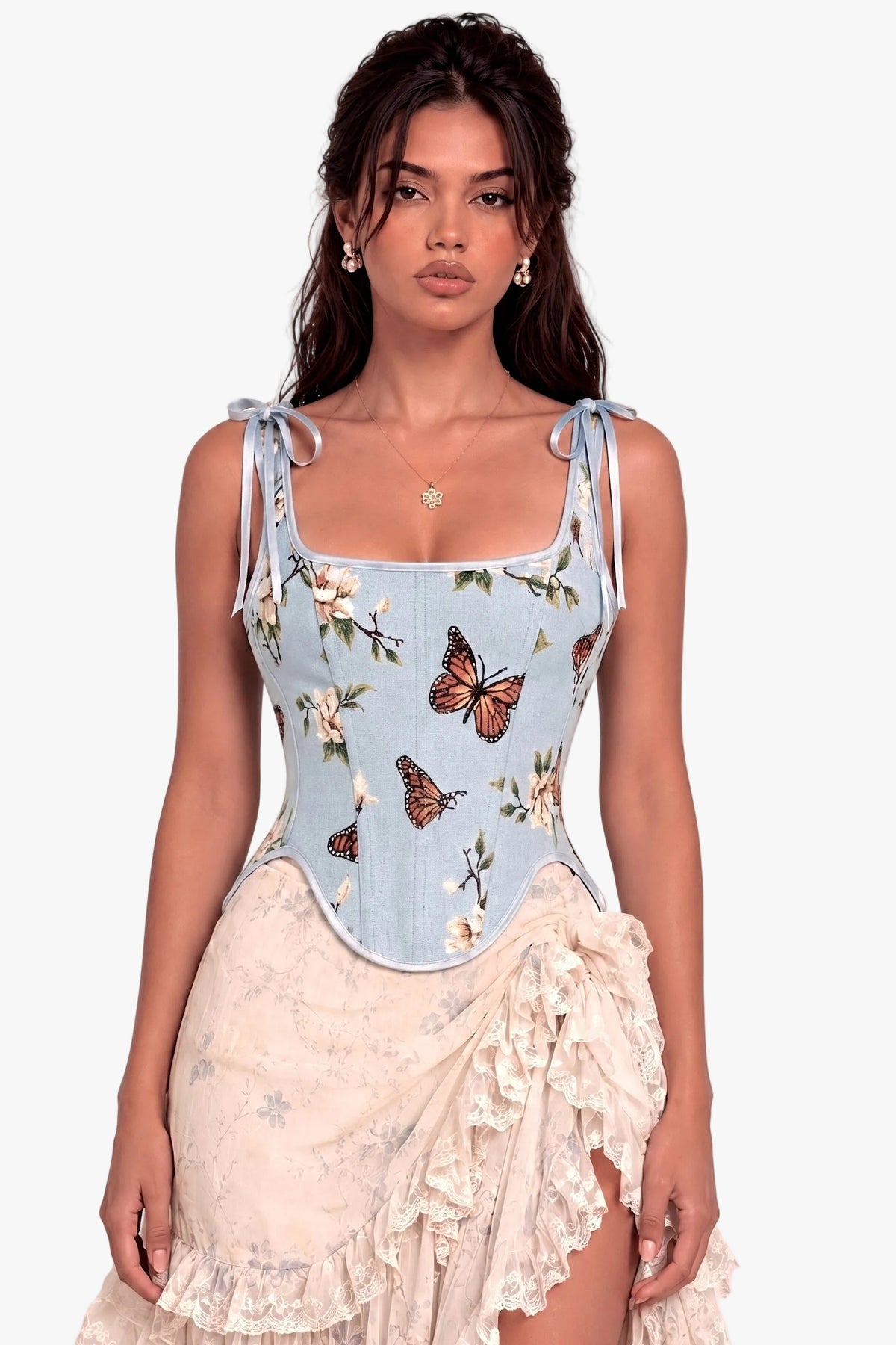 A woman modeling a light blue corset top with butterfly and floral prints, paired with a cream ruffled skirt, against a solid pale pink background.