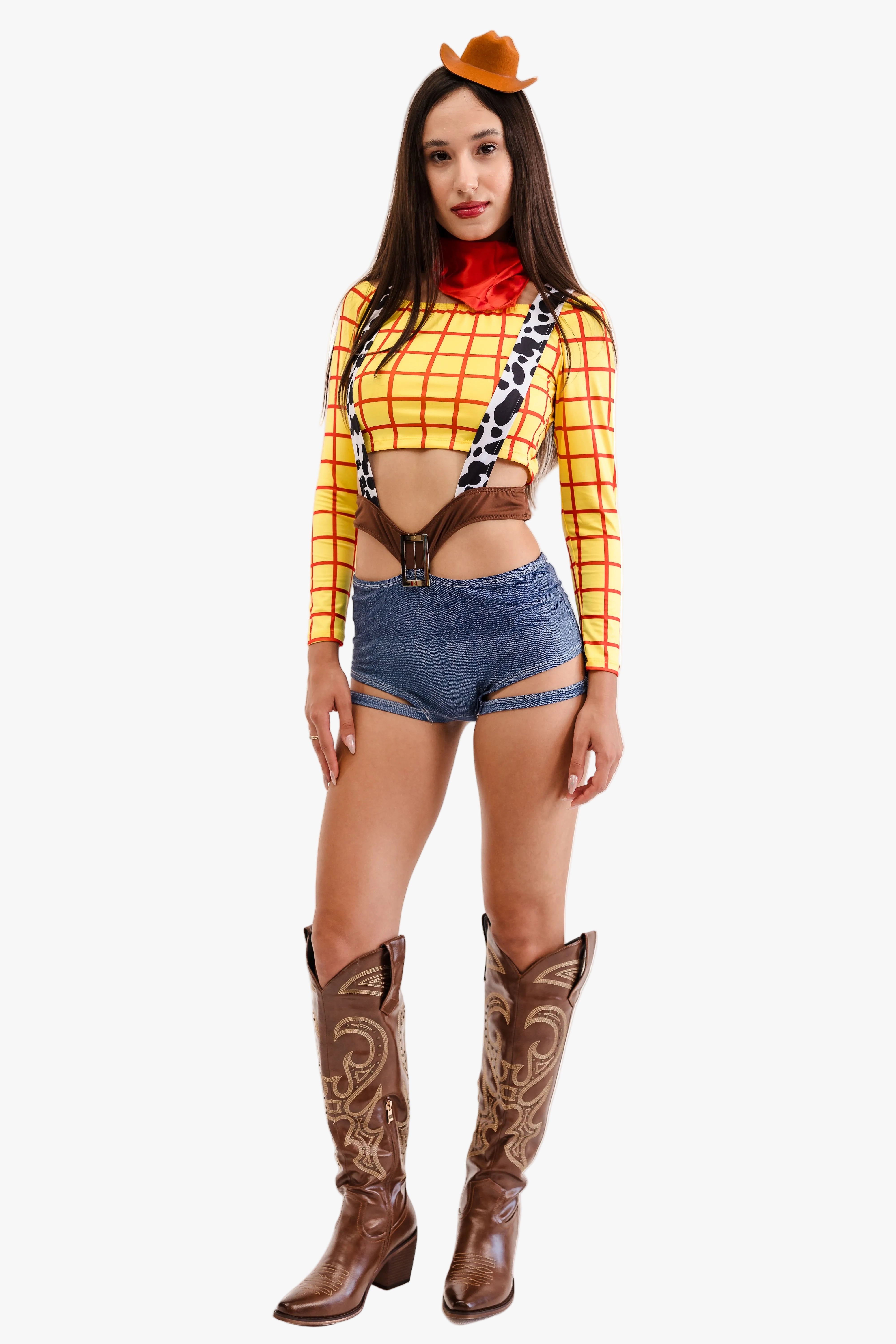 A woman modeling a Woody-inspired costume against a plain white background. The outfit includes a yellow and red plaid long-sleeve crop top, blue denim shorts, brown suspenders, a red neck scarf, brown cowboy boots, and a small brown hat.
