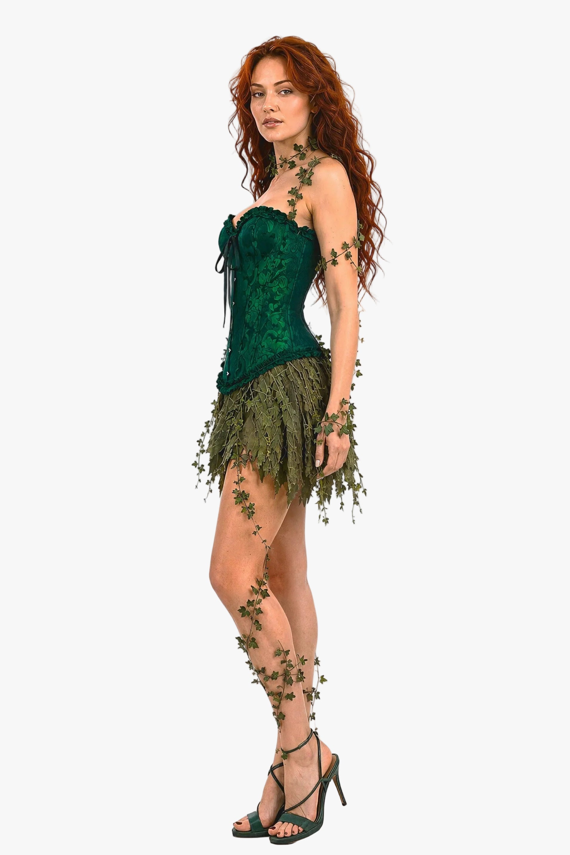 A model with long wavy red hair poses in a green lace strapless corset top and a matching leafy fringe skirt, adorned with vine and leaf embellishments, against a white studio background.