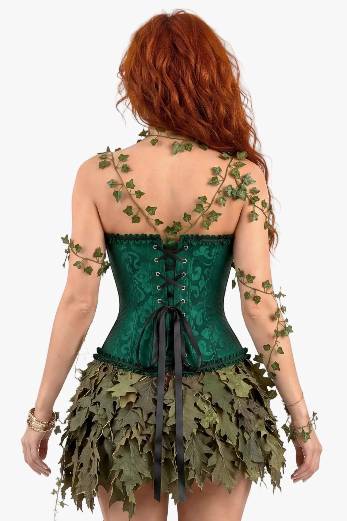 A woman with long red hair is shown from the back wearing a green lace corset top and a leafy skirt, with green ivy vines draped over her shoulders and arms, against a plain white background.