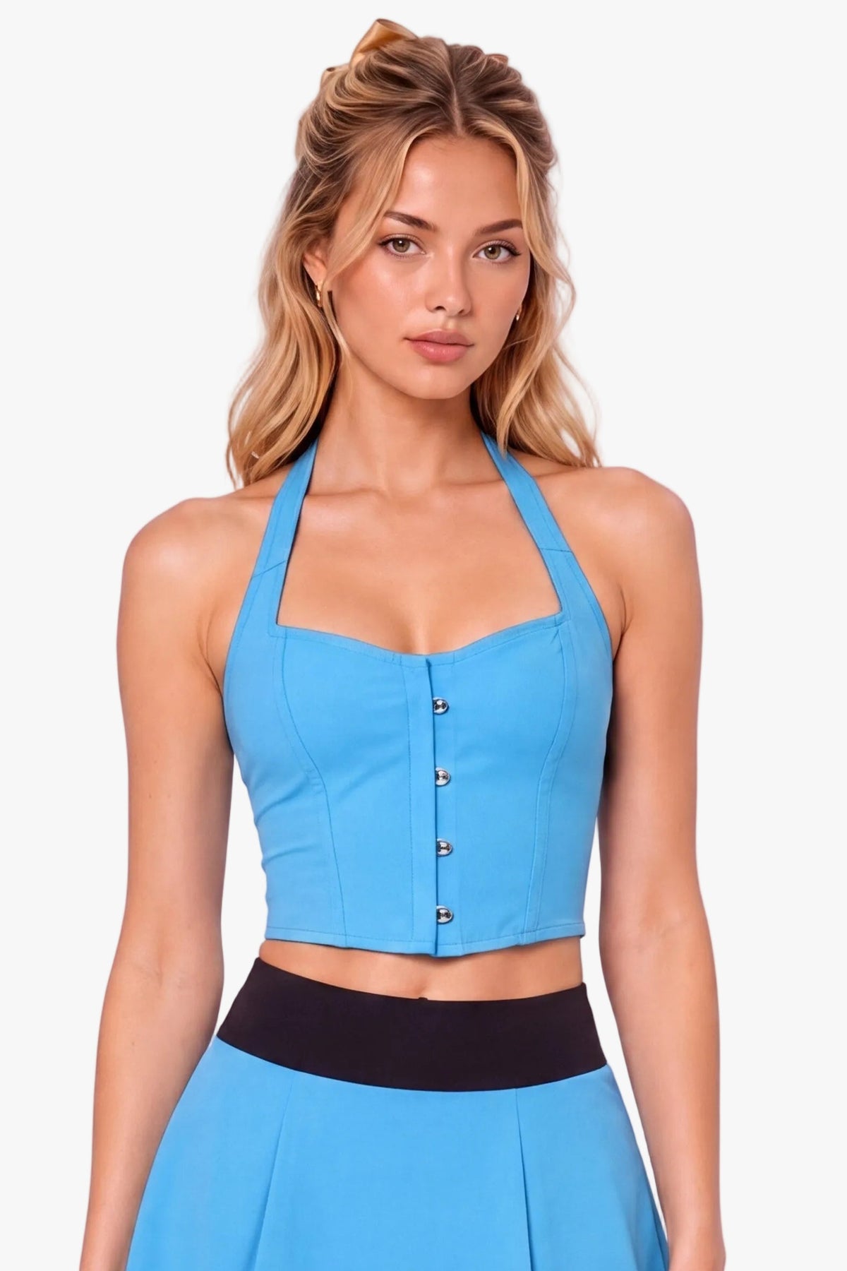 A woman modeling a bright blue halter crop corset top and matching pleated mini skirt set with a black waistband, styled with white socks and black Mary Jane shoes against a light lavender studio background.