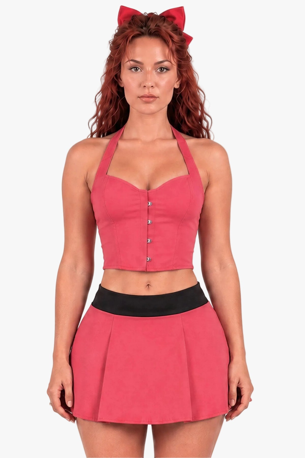 A woman modeling a powerpuff girl blossom costume - a pink two-piece outfit consisting of a halter crop corset top with silver buttons and a matching pleated mini skirt with a black waistband, accessorized with a red bow headband against a light gray background.