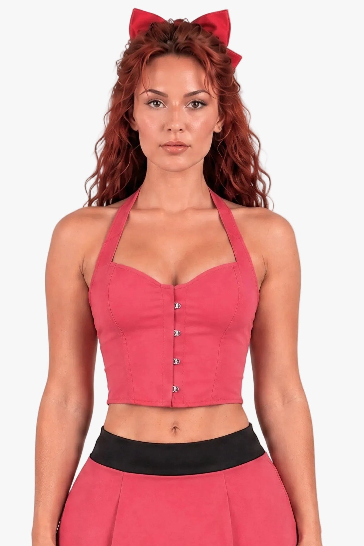 A woman modeling a powerpuff girl blossom costume - a pink two-piece outfit consisting of a halter crop corset top with silver buttons and a matching pleated mini skirt with a black waistband, accessorized with a red bow headband against a light gray background.