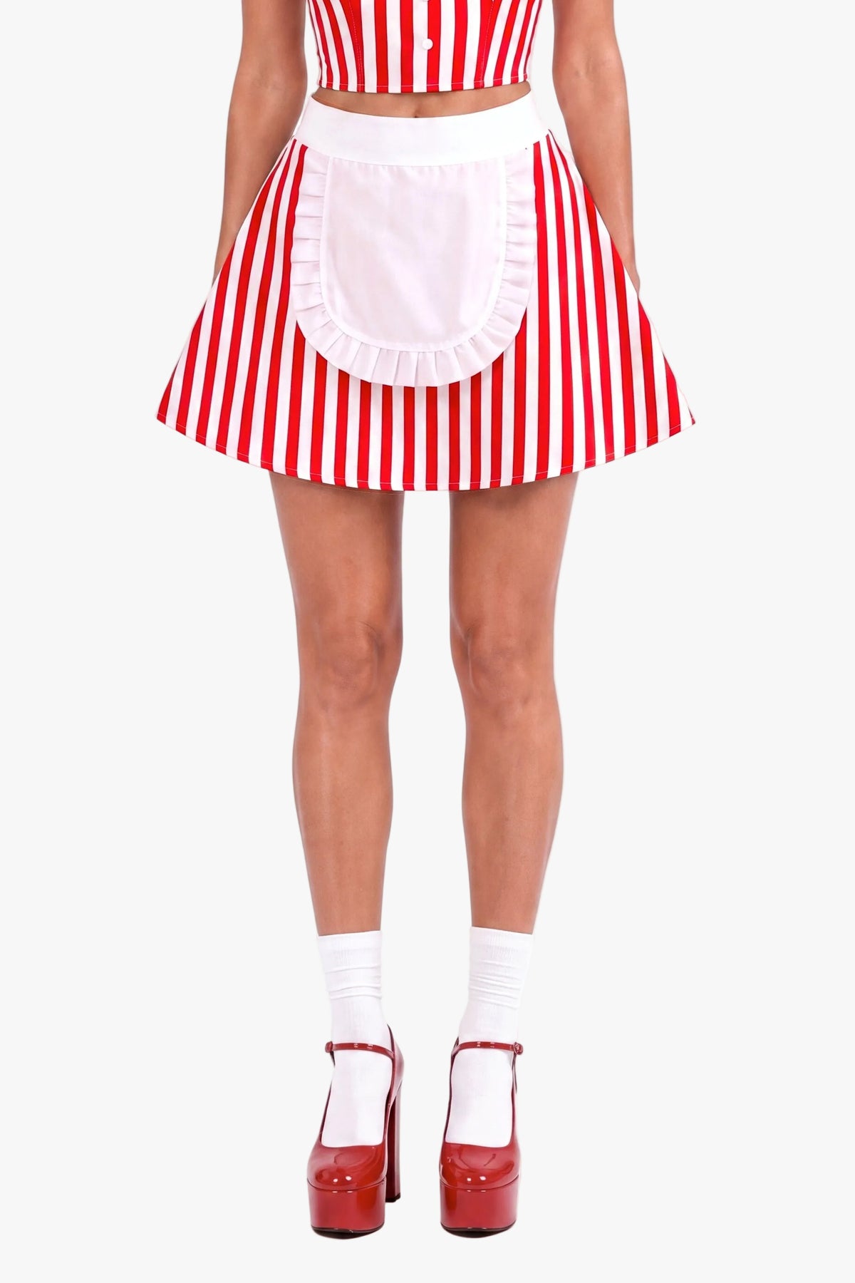 A woman modeling a red and white vertically striped diner costume set consisting of a halter crop top, matching skirt, and a white apron with a ruffled hem. She is wearing a name tag that says 'Sally' against a plain white background.