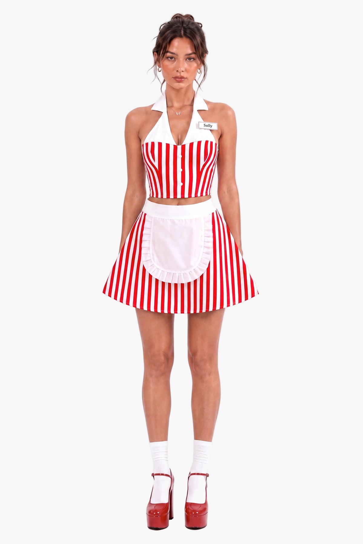 A woman modeling a red and white vertically striped diner costume set consisting of a halter crop corset top, matching skirt, and a white apron with a ruffled hem. She is wearing a name tag that says 'Sally' against a plain white background.