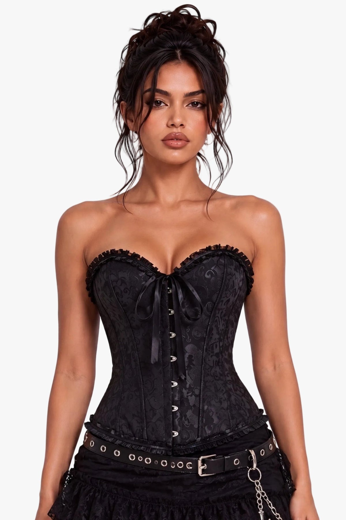 A model wearing a black lace and satin corset mini dress with a ruffled skirt, studded belt, and cross chain accessory, set against a plain light gray studio background.