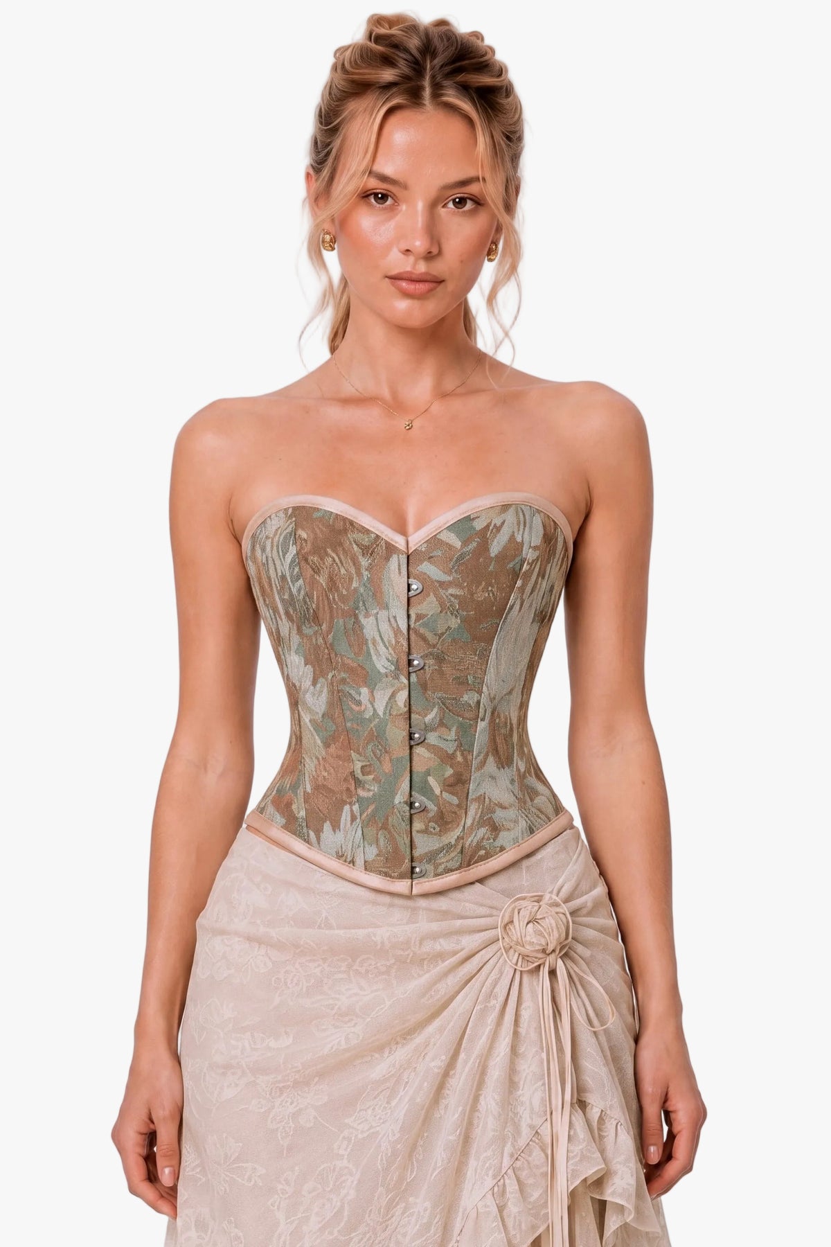 A woman modeling a strapless corset-style top with a muted floral pattern in beige, taupe, and olive tones, paired with a light beige draped skirt, against a plain light gray studio background.