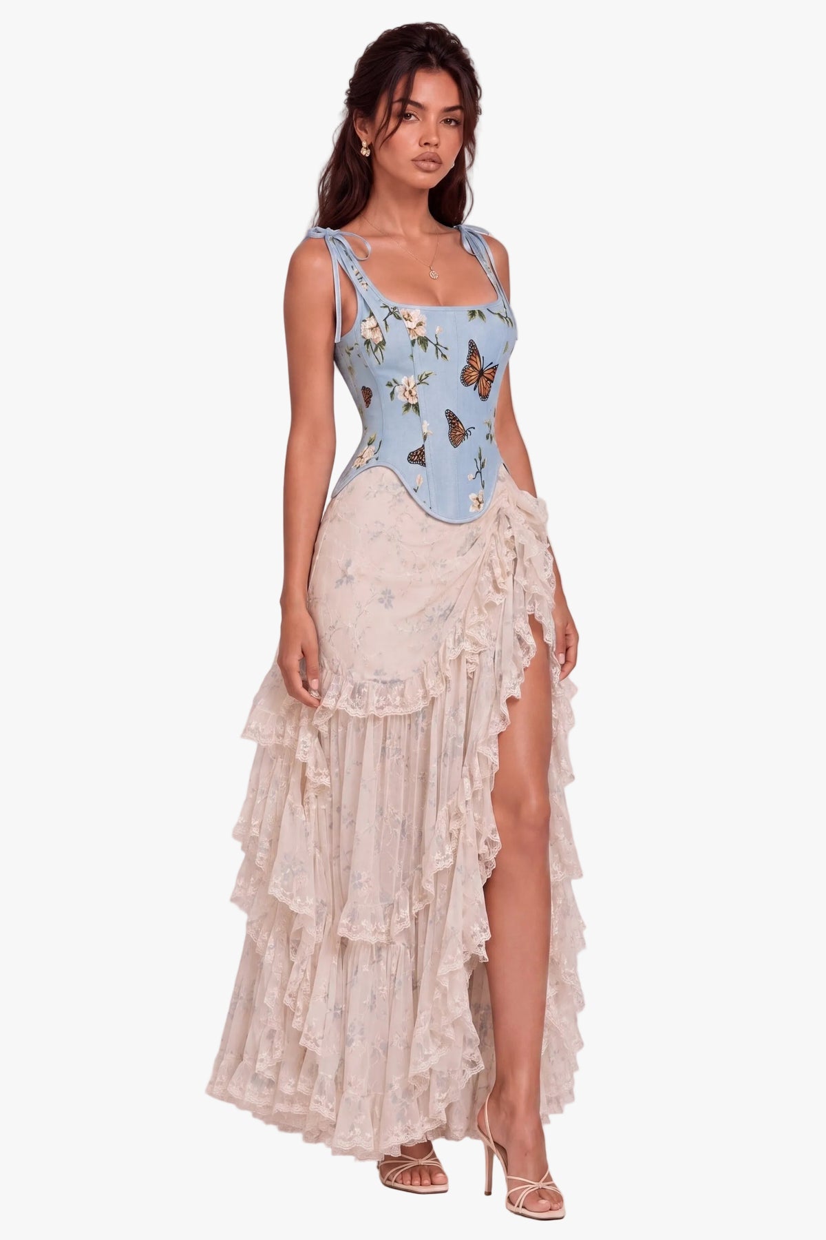A model wearing a light blue sleeveless corset bustier top with a butterfly print and a long, ruffled cream-colored skirt, standing against a neutral light gray studio background.