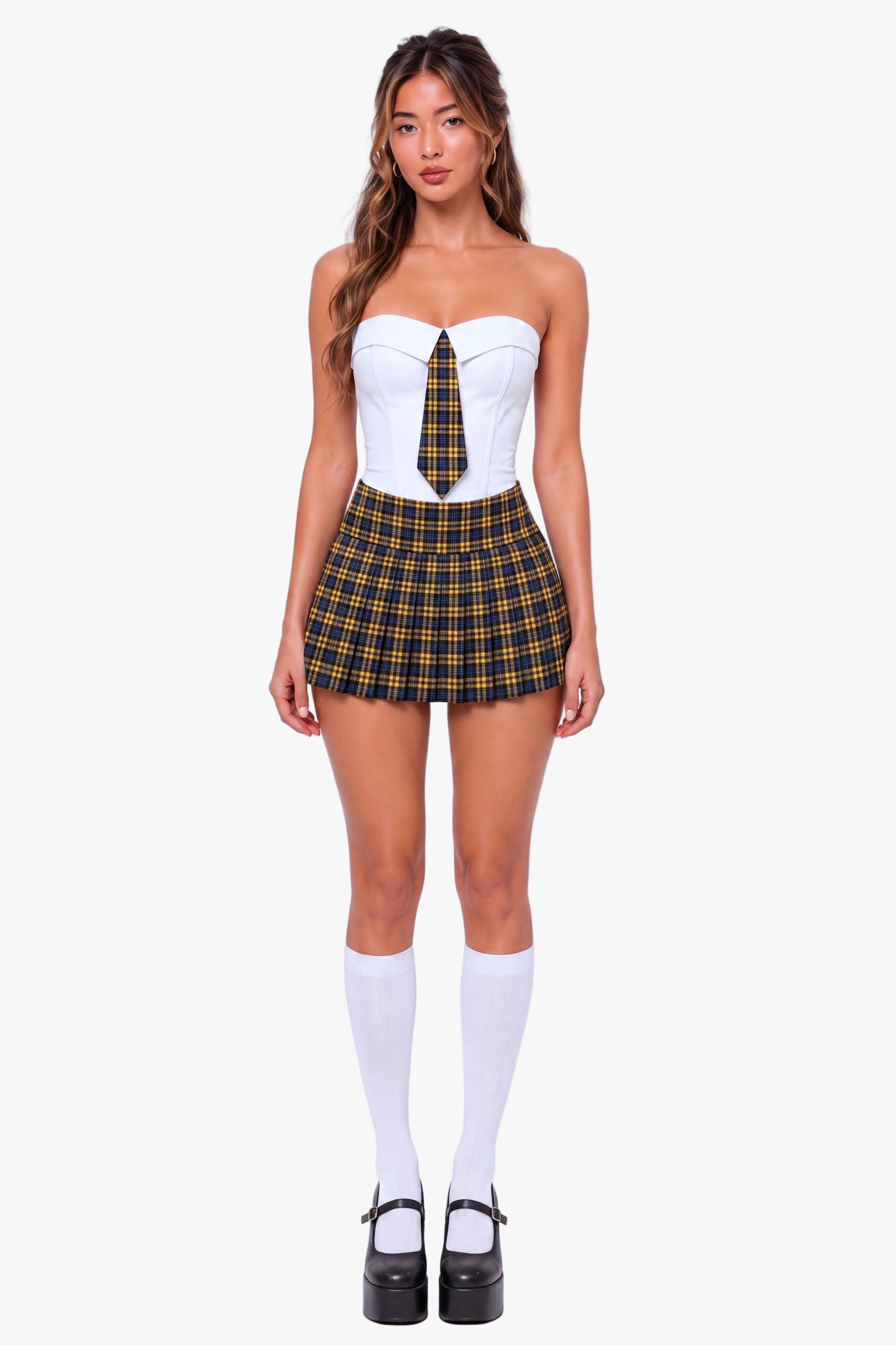 A model stands against a light gray studio background wearing a schoolgirl-inspired outfit consisting of a white strapless corset top with a yellow and black plaid necktie, a matching plaid mini skirt, white knee-high socks, and black Mary Jane platform heels.
