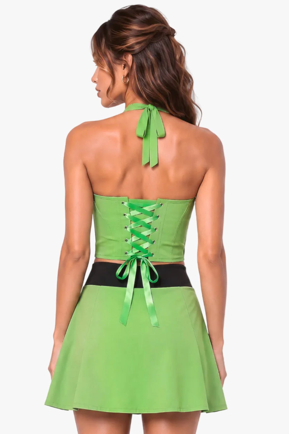 A woman shown from the back wearing a bright lime green halter mini dress with a lace-up corset-style back and a black waistband, against a pale pink studio background.