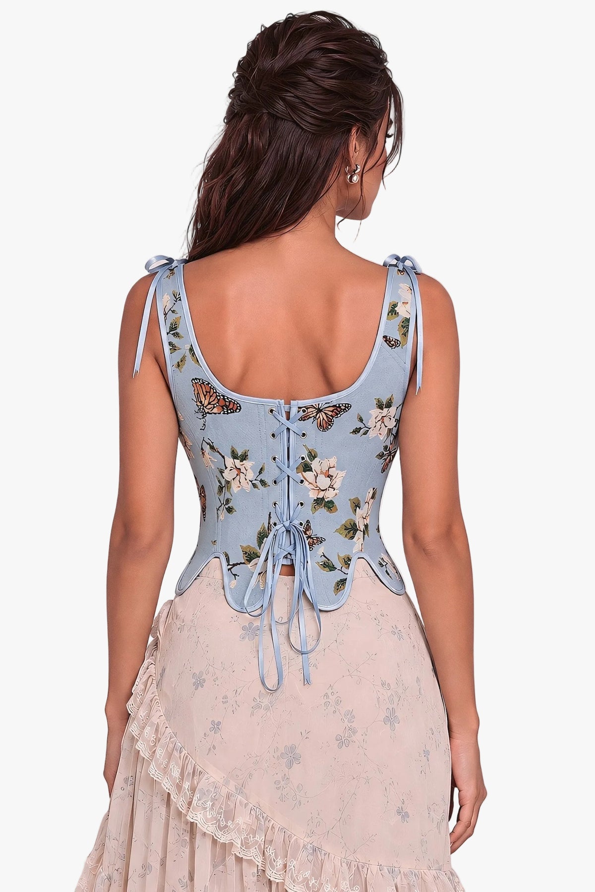 A woman shown from the back wearing a light blue floral corset with butterfly and floral embroidery, paired with a pale pink ruffled skirt, against a soft neutral studio background.