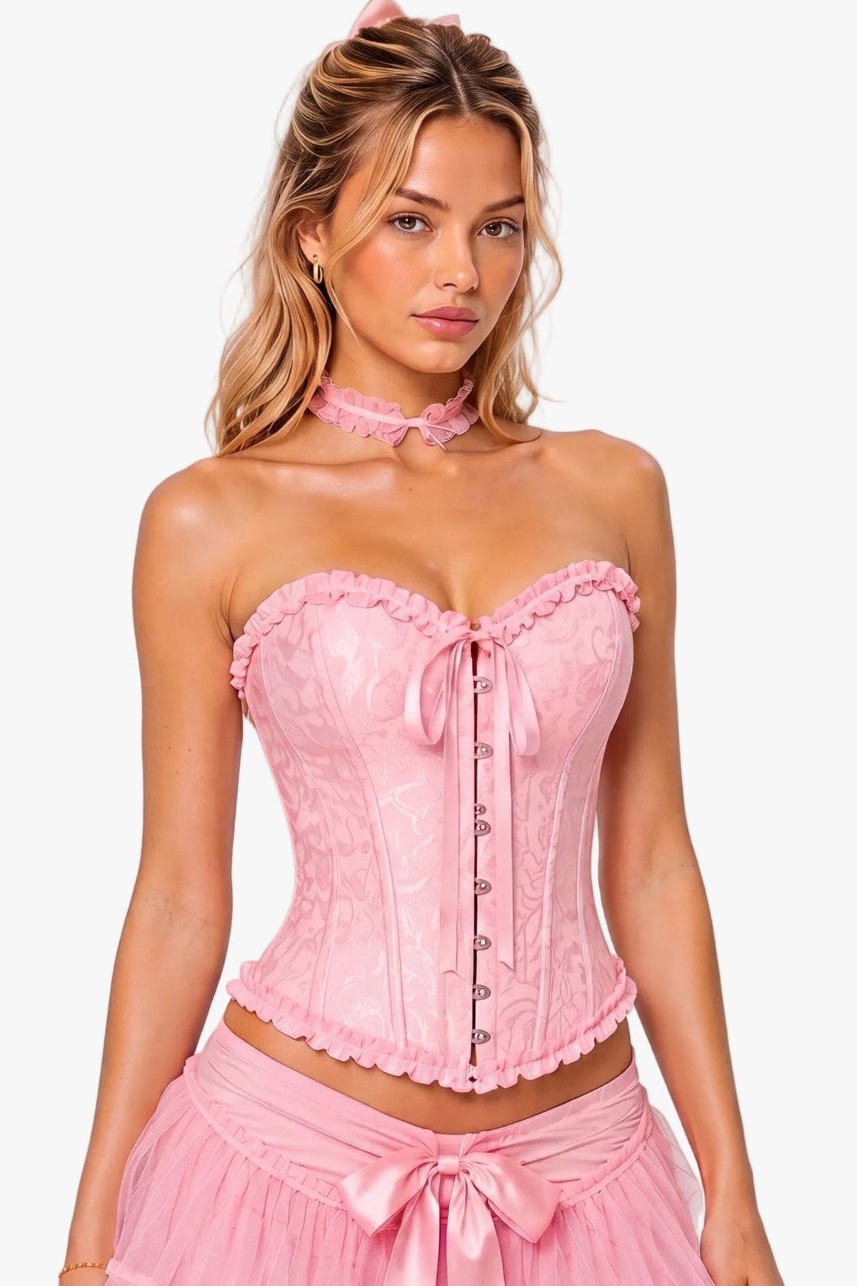 A woman modeling a pink princess peach costume consisting of a lace corset top with a sweetheart neckline, matching ruffled tulle mini skirt with a front bow, and a matching pink choker collar, against a light gray studio background.