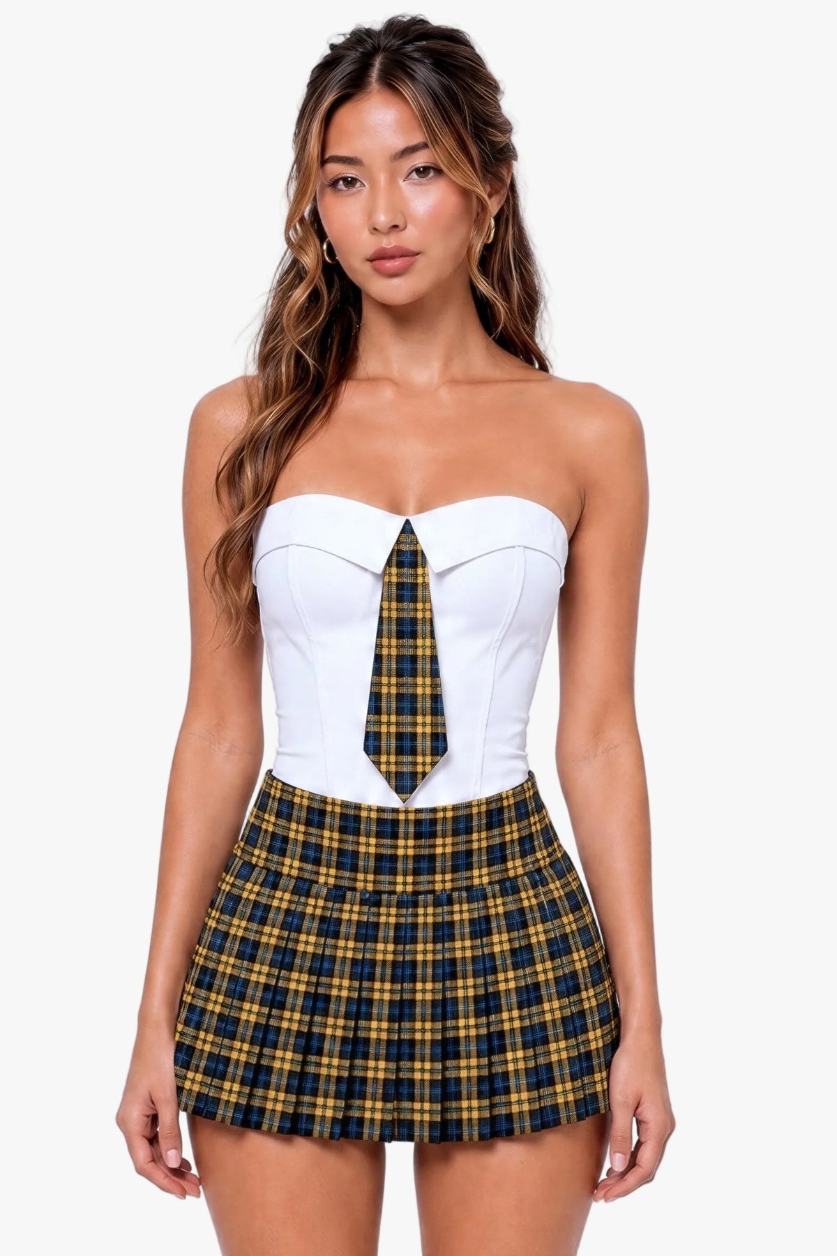 A woman modeling a strapless sweetheart corset top in white with a yellow and navy plaid tie detail at the center, paired with a matching plaid pleated mini skirt, against a light gray studio background.