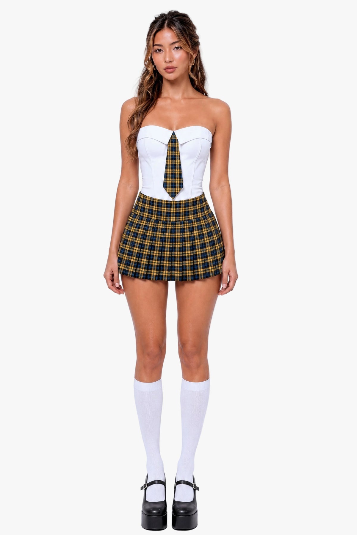 A model stands against a light gray studio background wearing a strapless white corset-style top with a yellow and black plaid tie detail, matching plaid mini skirt, white knee-high socks, and black platform Mary Jane shoes.