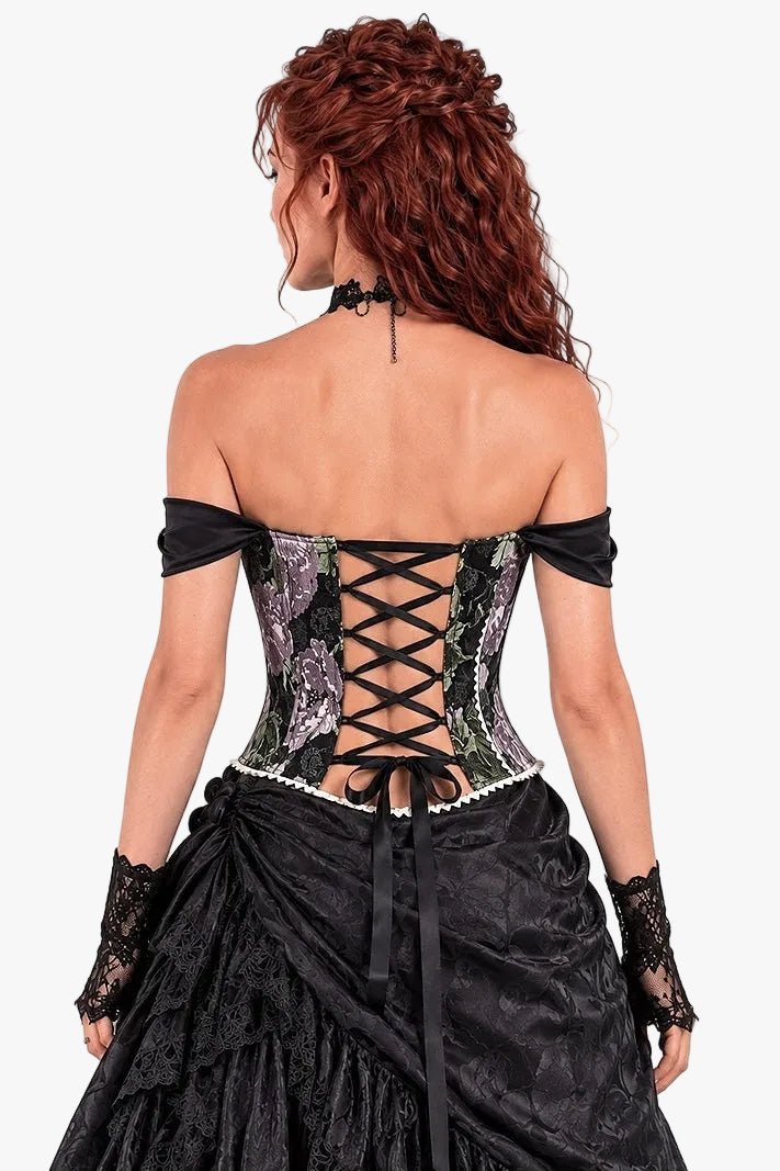 A woman shown from the back wearing a black off-the-shoulder gothic-style dress with a patterned corset and lace-up back, paired with a black ruffled skirt and lace gloves, against a plain white background.