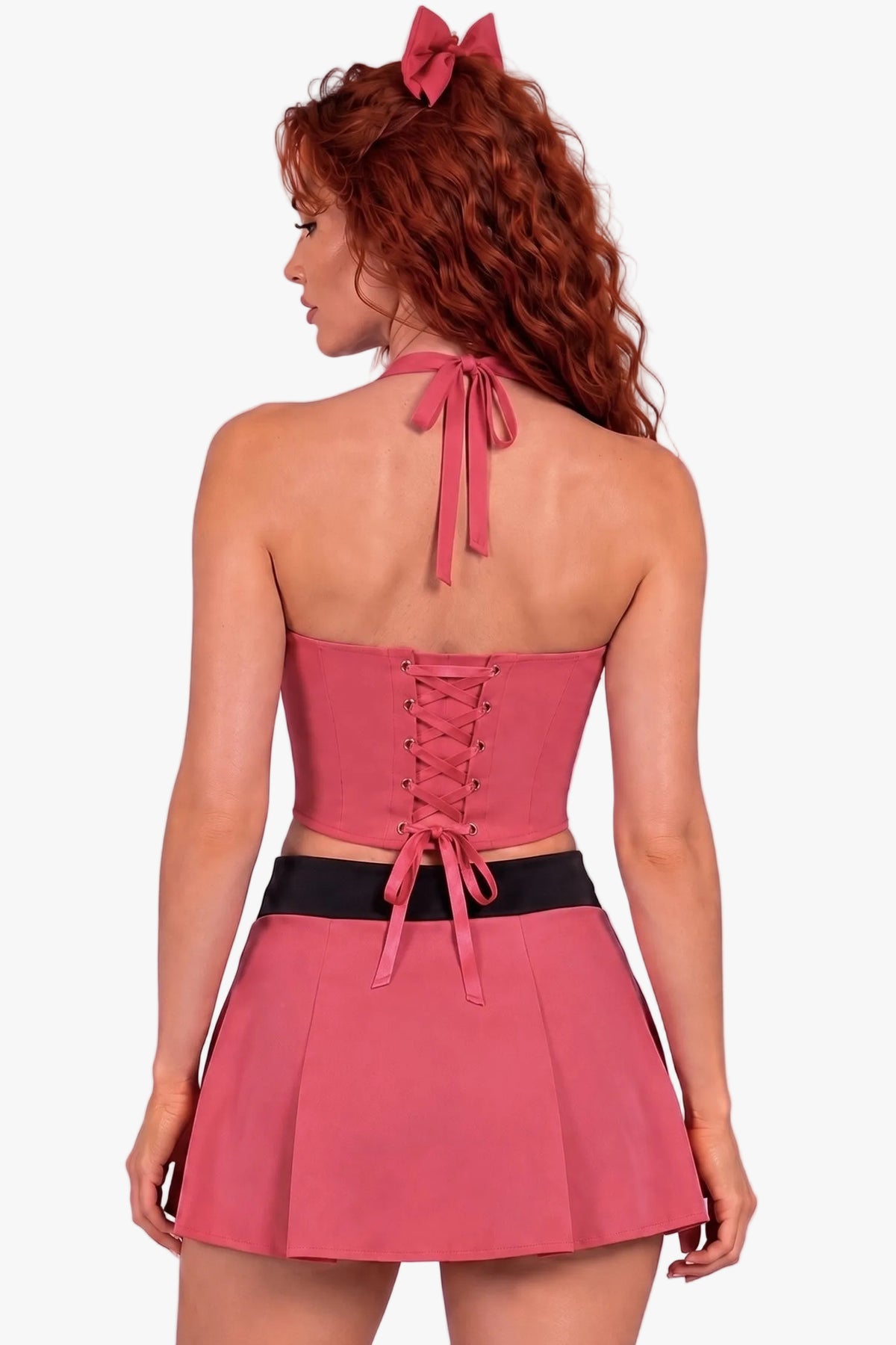 A woman with red hair wearing a pink halter mini dress with a black waistband, shown from the back against a solid lavender background.