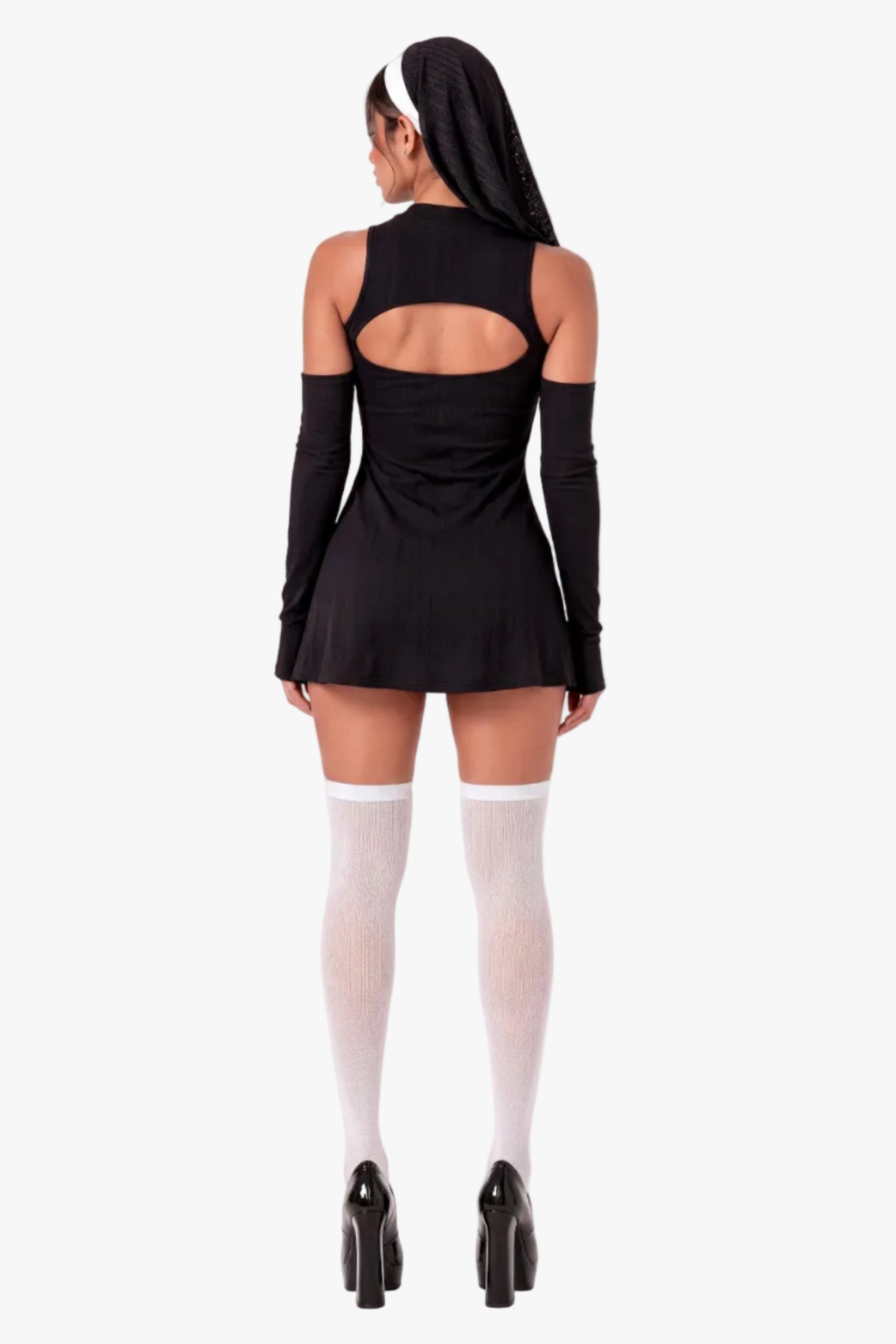 A model shown from the back wearing a black long-sleeve mini dress with a large cutout at the back, paired with white thigh-high stockings and black high heels, against a plain white studio background.