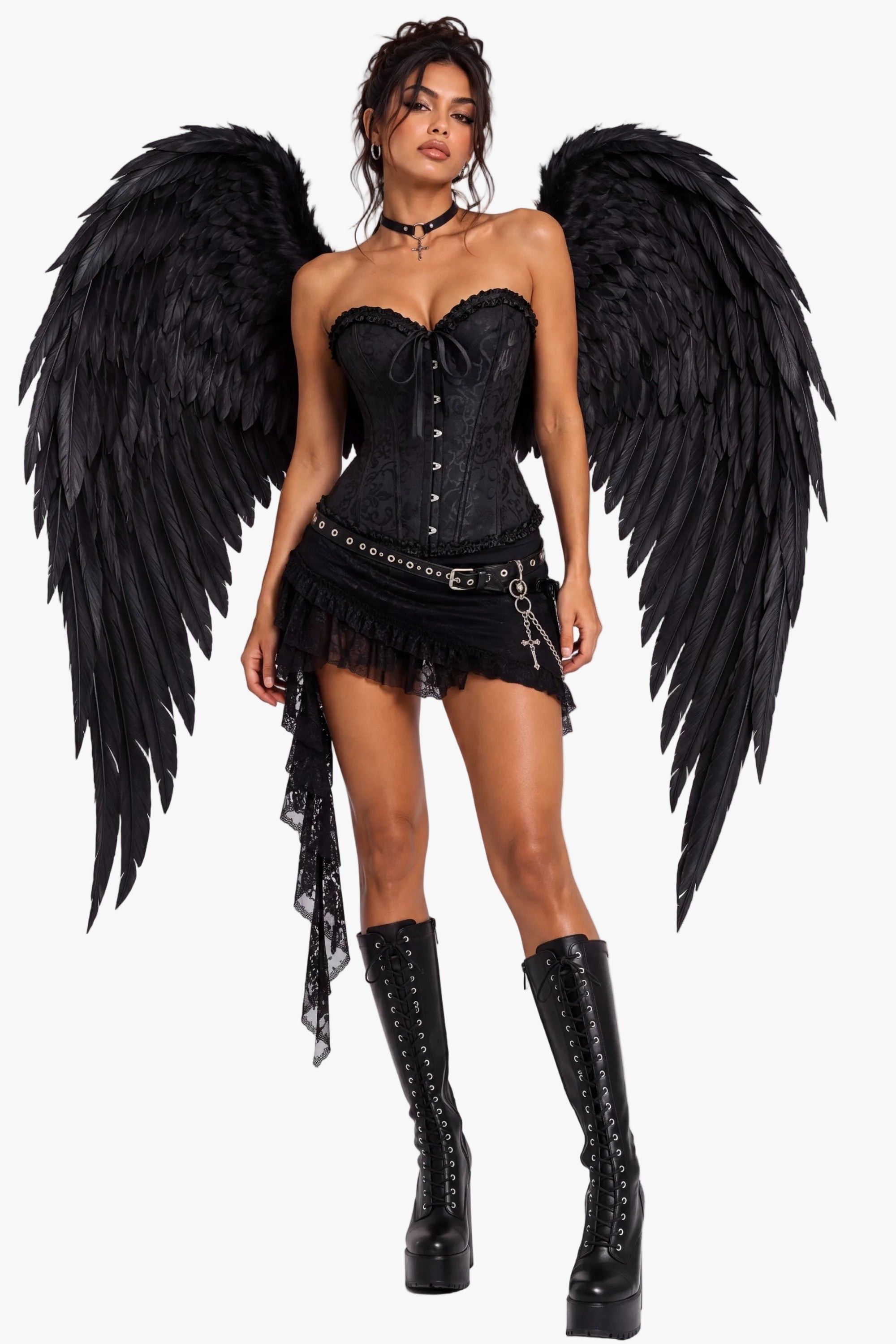 A model wearing a gothic black angel costume set, including large black feather wings, a black lace corset top, a fringed mini skirt with silver hardware, and black lace-up thigh-high boots, photographed against a plain light gray studio background.