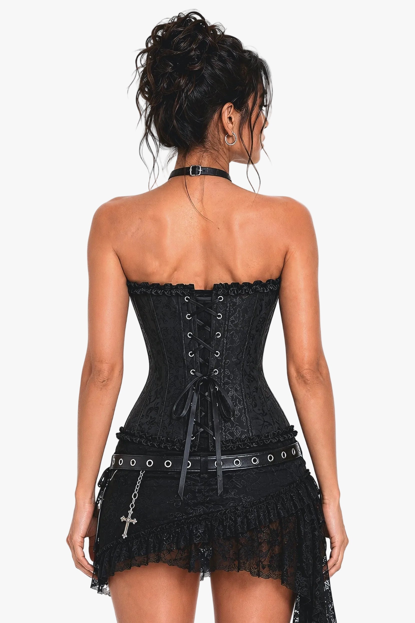A woman shown from the back wearing a black strapless lace corset mini dress with a lace-up back, ruffled trim, and a long dangling lace tail. She is photographed against a plain light gray studio background.