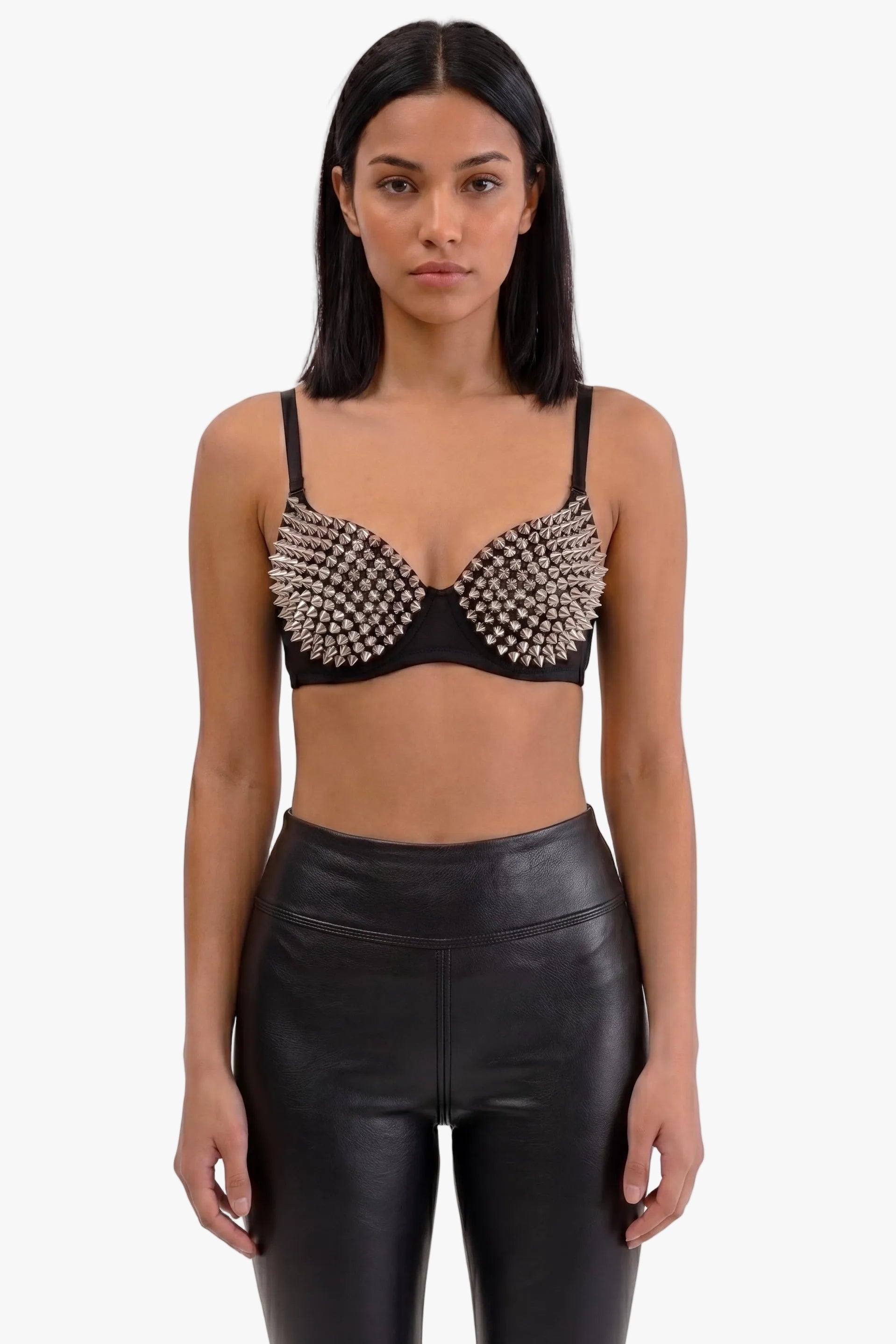 A model wearing a black bralette top heavily embellished with silver rhinestones, paired with black faux-leather pants, against a plain white background.
