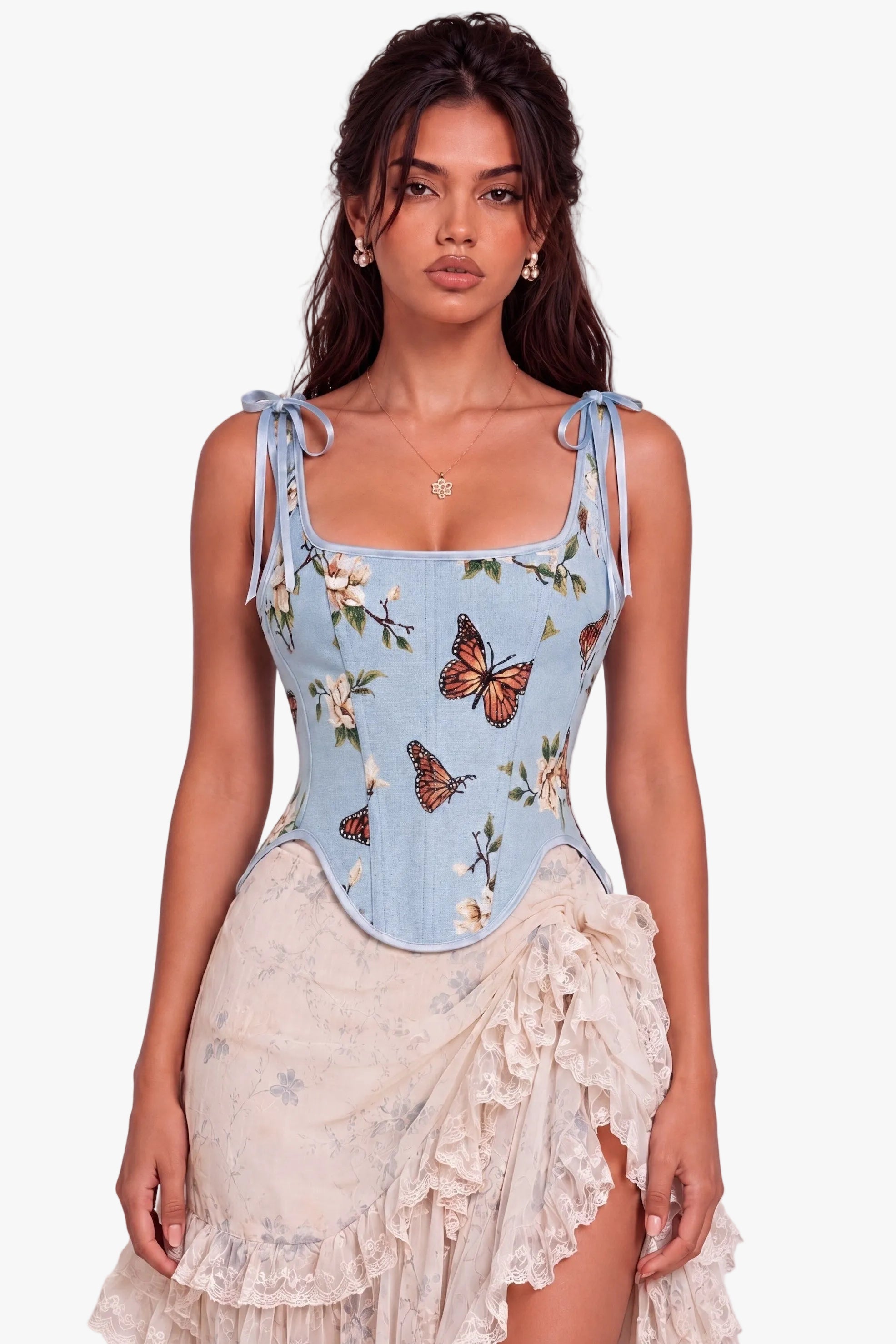 A model wearing a light blue denim corset top with a butterfly and floral print, paired with a cream ruffled skirt, against a neutral studio background.