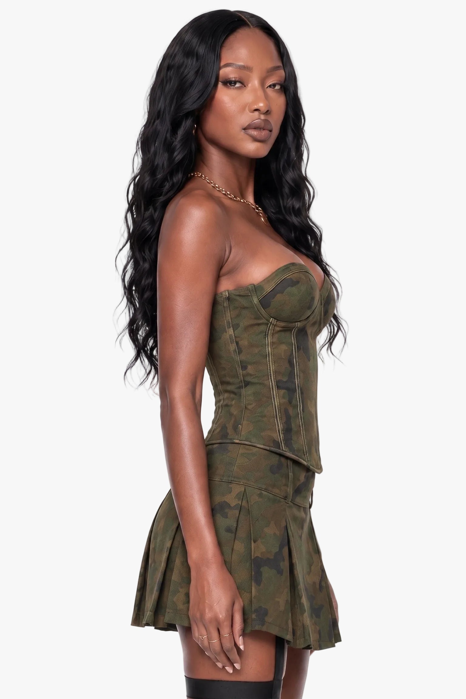 A woman modeling a strapless camouflage mini dress with a structured corset-style bodice and pleated skirt, shown against a plain light gray studio background.