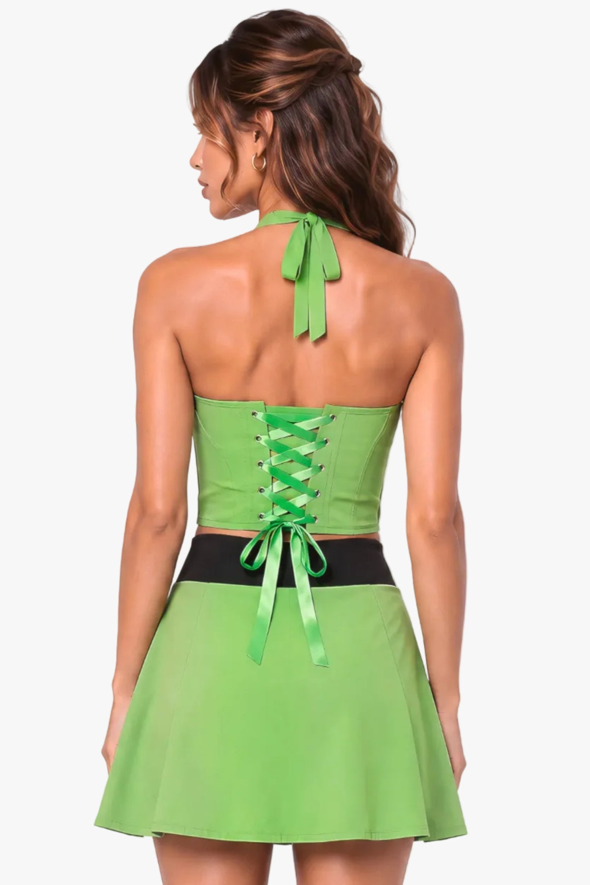 A woman shown from the back wearing a bright lime green halter mini dress with a lace-up corset-style back and a black waistband, against a pale pink studio background.
