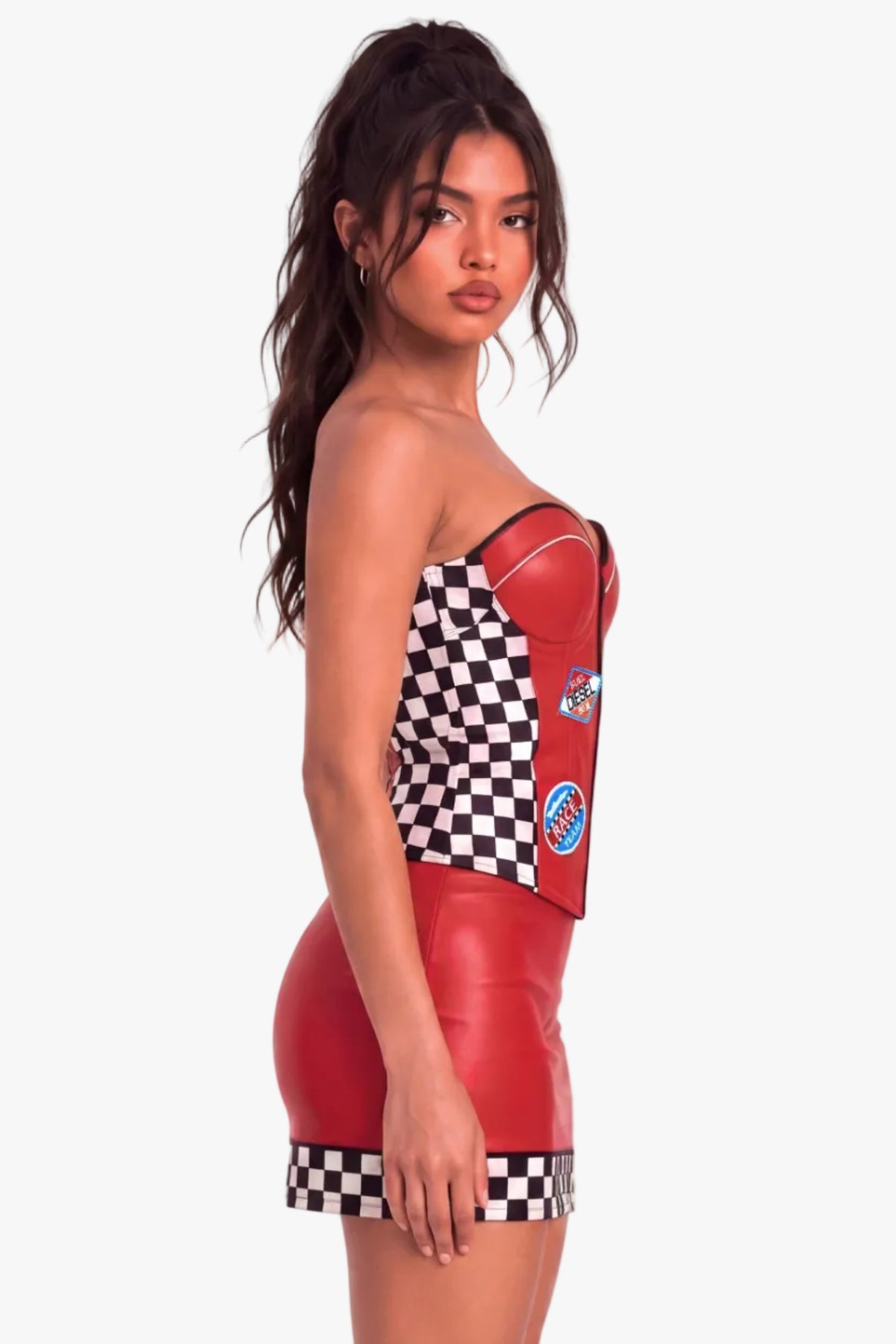 A woman modeling a strapless red faux-leather corset top with a black-and-white checkered bodice and hem, featuring racing-style patches on the side, against a plain white studio background.